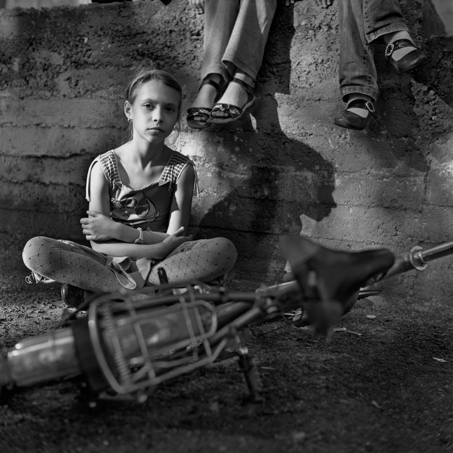 Black-and-white street portrait of girl sitting behind old bycicle with friends taken on medium format film camera Yashica Mat G124