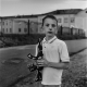 Dramatic black-white portrait of boy with dirty face handling toy machine gun in his hands with school building in background, Minsk city, Belarus