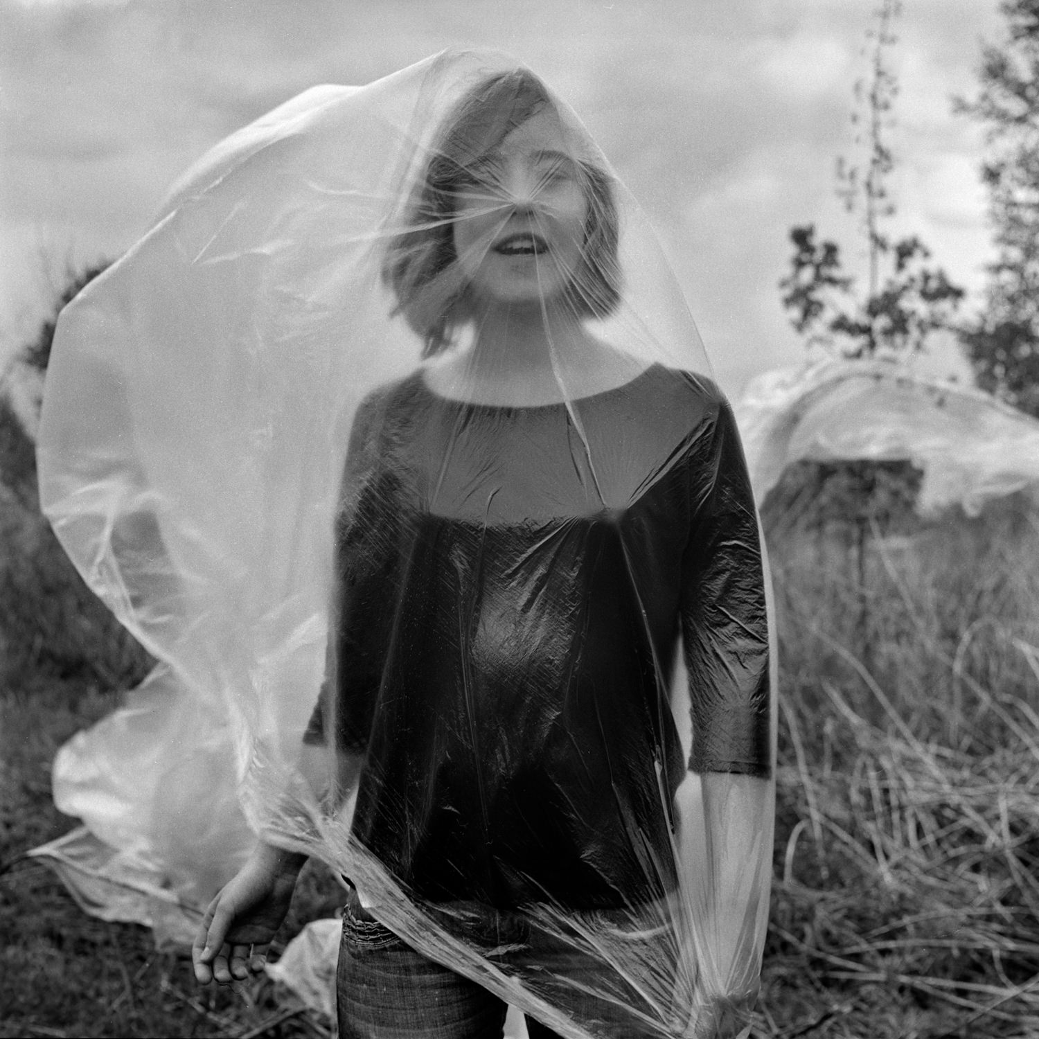 Emotional portrait of a laughing girl in the garden with a plastic bag flying out into the wind, covering the whole body